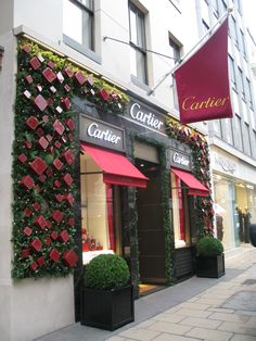 the outside of a store with red awnings and plants on the side walk