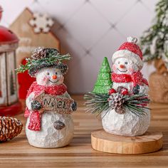 two snowmen are standing next to each other on a wooden board with pine cones