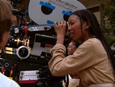 a woman standing in front of a camera on top of a movie set with other people around her