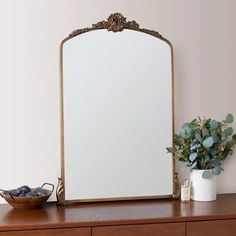 a mirror sitting on top of a wooden dresser next to a vase with flowers in it