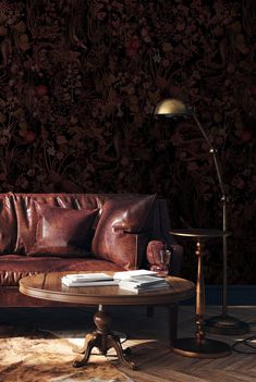 a brown leather couch sitting on top of a wooden floor next to a table and lamp