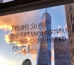 there is a message written on the window in front of skyscrapers that say, dreams so big you get uncomfortableable telling small minds people