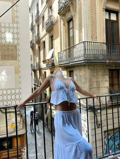 a woman is standing on a balcony with her arms outstretched and looking at the street