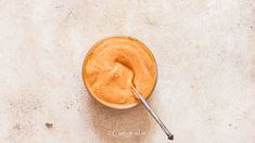 a spoon in a glass filled with peanut butter on top of a white countertop