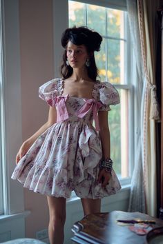 a woman standing in front of a window wearing a dress with ruffles on it