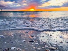 the sun is setting over the ocean with small shells on the sand and in the water