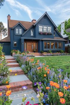 a blue house with lots of flowers in the front yard and steps leading up to it