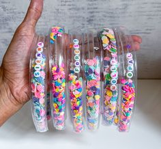 a hand is holding several bracelets with beads on them in clear plastic cases, which are decorated with letters and flowers