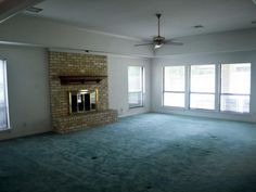 an empty living room with large windows and a fireplace in the center, surrounded by blue carpet