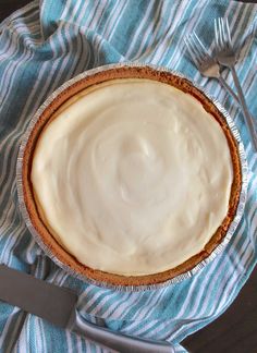 a pie with frosting in a bowl on a blue and white towel next to a fork