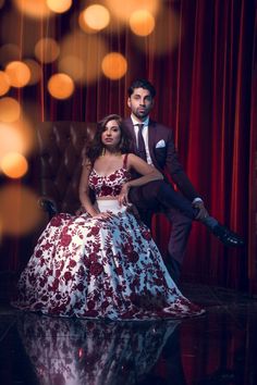 a man and woman sitting on a chair in front of a red curtain with lights