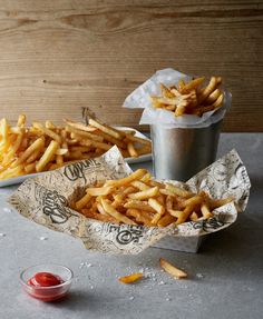 french fries in paper wrappers with ketchup next to them on a table