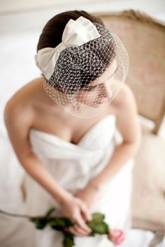 a woman wearing a veil and holding a rose in her hand while sitting on a bed