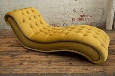 a yellow chaise lounger sitting on top of a wooden floor next to a brick wall