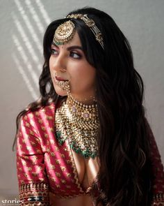 a woman in a red and gold outfit with jewelry on her face, looking off to the side