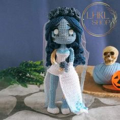 a crocheted doll is holding a piece of paper next to a skull and pumpkin