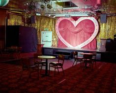 a stage set up with chairs, tables and a heart shaped curtain