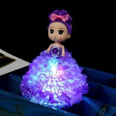 a little doll sitting on top of a purple light in a blue box with pictures next to it