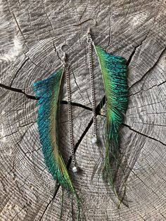 two pairs of peacock feathers hanging from chains on a piece of tree trunk with beads attached to them