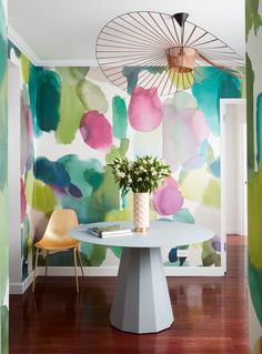 a table with a vase on it in front of a wall painted with watercolors