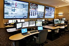 an office with multiple monitors and laptops on the desk in front of large screens