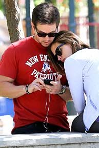 a man and woman sitting on a bench looking at a cell phone together, with one holding the other's head