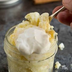 a person scooping some food out of a small glass jar with whipped cream on top