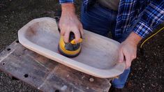 a man using a sanding tool on a piece of wood in a tray that is sitting on the ground