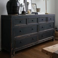 an old black dresser with many drawers and pictures on it's top, next to a wooden bench