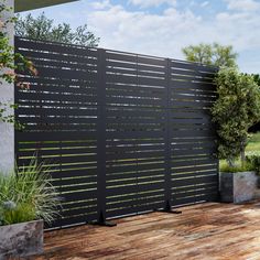 a wooden deck next to a black fence and some plants on the side of it