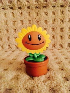 a toy sunflower sitting on top of a brown pot filled with green leaves and smiling