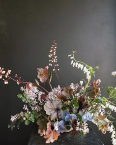 a vase filled with lots of flowers on top of a black table next to a wall