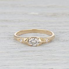 a yellow gold engagement ring with three diamonds on the top and bottom, sitting on a piece of wood