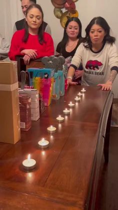 a group of people sitting around a table with candles on it and boxes in the background