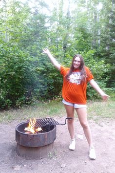 a woman standing in front of an open fire pit with her arms spread wide out