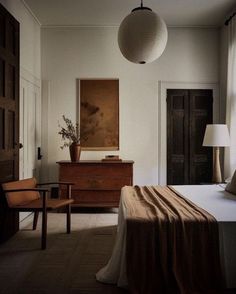 a bedroom with a bed, two chairs and a lamp hanging from the ceiling above it