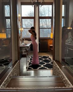 a woman standing in front of a window looking into a room with a chandelier hanging from the ceiling