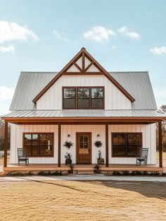 a white and brown house with two chairs on the front porch next to grass field