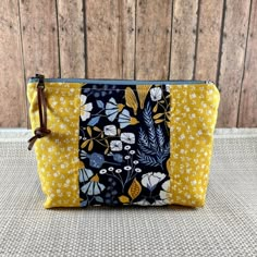 a yellow and black floral print zippered pouch with brown leather handles on a wooden background