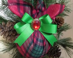 a christmas ornament hanging from a tree with pine cones and green ribbon on it