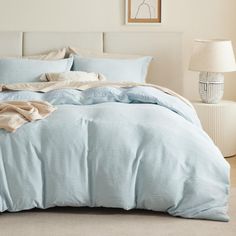 a bed with blue comforter and pillows in a white room next to a lamp