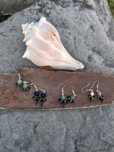 five pairs of earrings sitting on top of a piece of wood next to a seashell