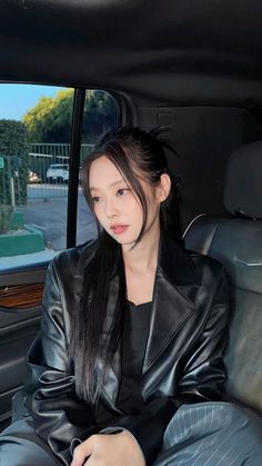 a woman sitting in the back seat of a car with long black hair and wearing a leather jacket