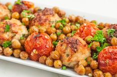 a white plate topped with meat covered in tomatoes and garbanzo beans next to a fork