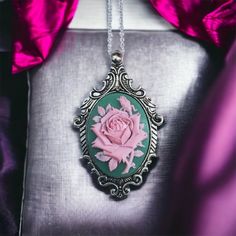 Styled in a majestic fashion with a feminine twist, the Victorian Rose Cameo Necklace is sure to make a statement! Featuring a beautifully detailed cameo with an pink rose on a green resin background.  The Victorian Rose Cameo Necklace is set in a  vintage-style antique silver-plated large pendant. The pendant measures approximately 2.5" long and 2" wide.   Add on a nice antique silver-plated satellite bead chain, that closes with a lobster clasp, and may be added at checkout. Choose your own ne Elegant Pink Rose Necklace, Pink Rose Pendant Jewelry, Pink Rose Design Pendant Necklace, Pink Cameo Necklace For Gifts, Resin Background, Pink Victorian, Floral Pendant, Cameo Necklace, Bead Chain