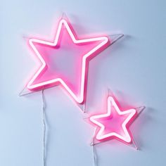 two neon pink star shaped lights on a white wall next to each other with string