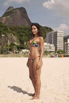 a woman standing on top of a sandy beach next to a tall mountain in the background