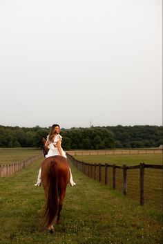 a woman riding on the back of a brown horse across a lush green field next to a wooden fence