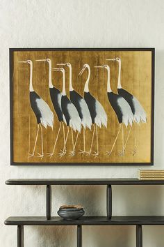 three birds are standing in front of a painting on the wall next to a shelf