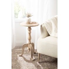 a small white table with a vase on it next to a chair in front of a window